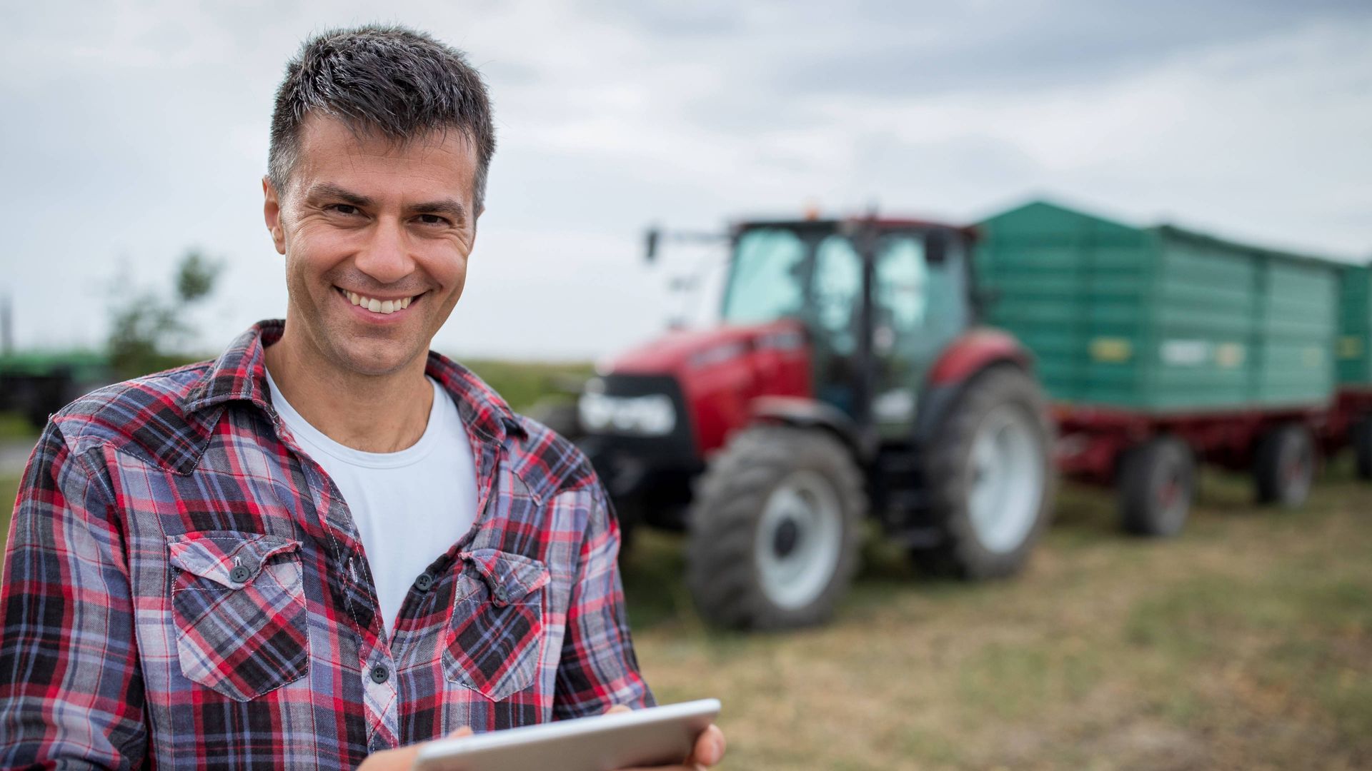 Image of a producer standing in front of a tractor with a tablet