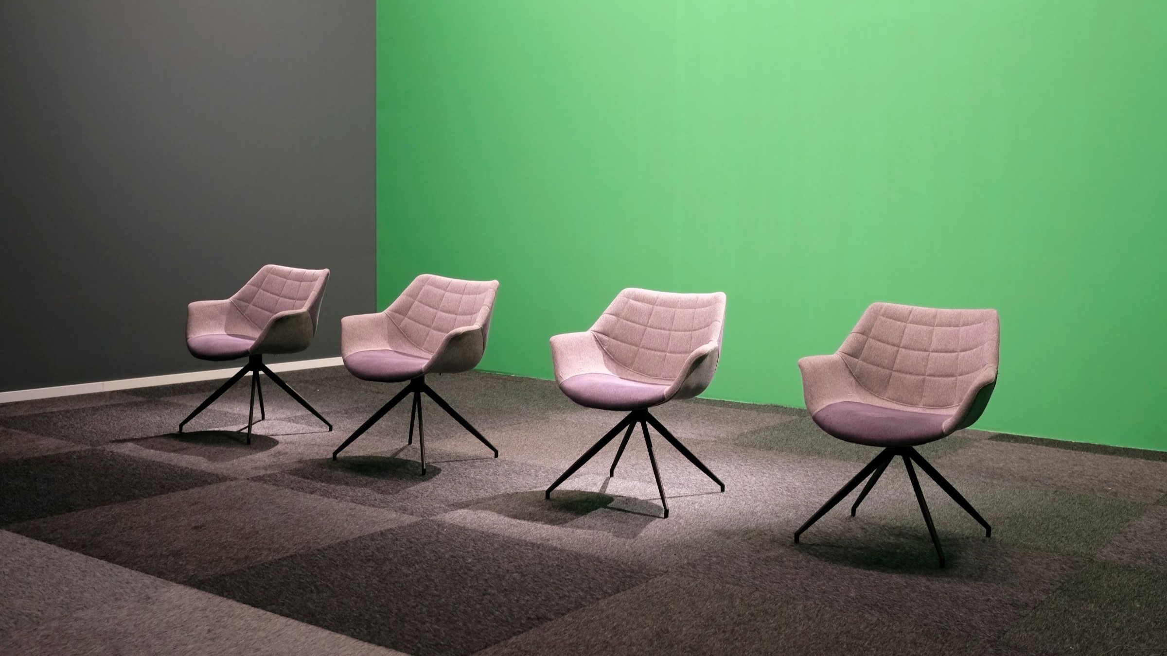 Symbolic image of a panel discussion showing four empty chairs in front of a green background.